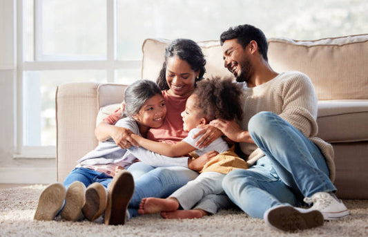 Family of four laughing together on the floor in front of a sofa